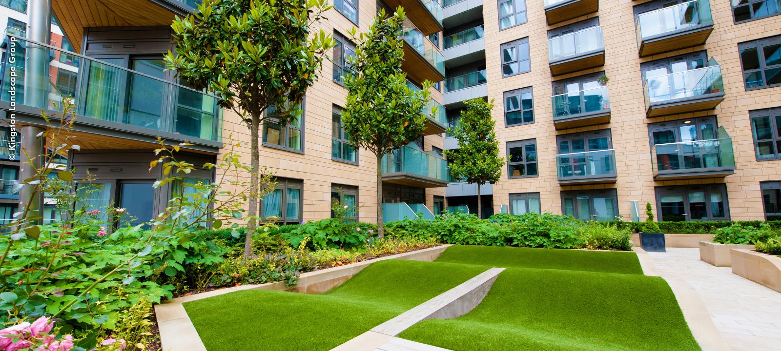 Lawn, small trees and plant beds surrounded by apartment blocks